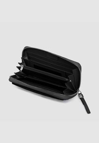 Portafoglio nero con cerniera a giro realizzato in pelle strutturata, con molteplici fessure per carte, due scomparti e una fodera liscia. Dettagli in metallo color argento.