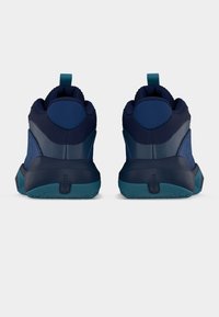 Ζευγάρι αθλητικών παπουτσιών σε ναυτικό και τιρκουάζ χρώμα, εμφανιζόμενα από πίσω, με επενδυμένους γιακάδες, θηλιές για τράβηγμα και υφή στις λαστιχένιες σόλες σε λευκό φόντο.