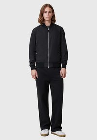 Schwarze Bomberjacke mit Reißverschluss, gerippten Bündchen und Saum. Kombiniert mit lockeren schwarzen Hosen und weißen Sneakern. Glatte Stofftextur.