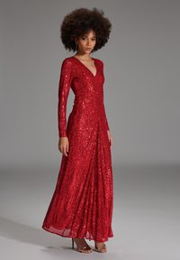Rode pailletten lange mouwen jurk met een V-hals en een aansluitend lijfje. Aangerimpelde rok met een zijopening en een gestructureerd glanzend oppervlak.