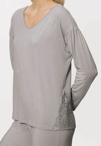 Jasnoszara bluzka z długim rękawem, wykonana z miękkiego materiału. Posiada dekolt w serek oraz skomplikowane koronkowe wykończenia po bokach. Prosty design z luźnym fasonem.