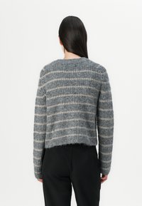 Γκρι πλεχτό πουλόβερ με μαλακή υφή, που διαθέτει οριζόντιες ρίγες σε ανοιχτό γκρι. Σύντομη, χαλαρή εφαρμογή με μακριά μανίκια και στρογγυλή λαιμόκοψη.