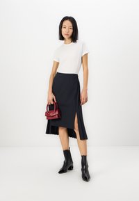 Tricou alb, fustă bleumarin cu deschidere laterală și detalii pliate, asortată cu o geantă mică roșie și cizme negre până la gleznă cu vârf ascuțit.