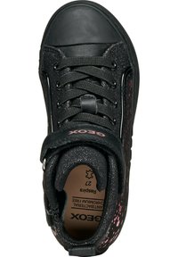 Zapatilla de tela negra con una puntera de goma, cordones texturizados y un diseño moteado en tonos rosas en el costado. Correa de velcro en el tobillo.