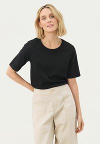 T-shirt nera a maniche corte con scollatura rotonda. Tessuto di cotone morbido, vestibilità comoda. Abbinata a pantaloni beige chiaro con tasche frontali.