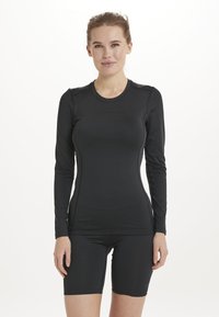 Zwarte sporttop met lange mouwen, een ronde hals, een nauwsluitend ontwerp en zachte stof; gecombineerd met zwarte shorts, wat een gecoördineerde outfit creëert.