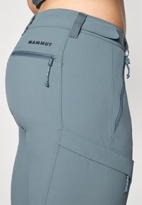Pantaloni azzurri chiari con vestibilità slim, realizzati in tessuto morbido, dotati di una tasca laterale con zip, logo sul retro e passanti per cintura per la regolazione.