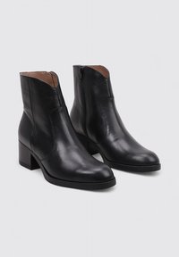 Botines de cuero negro con punta redonda, cremallera lateral y un tacón cuadrado moderado. Textura suave y diseño limpio.