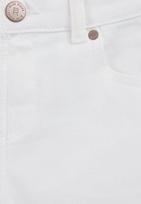 Blaga bijela denim tkanina izbliza s gumbom s oznakom "Blue Ridge" i vidljivim šavovima; glatka tekstura s suptilnim dijagonalnim uzorkom tkanja.