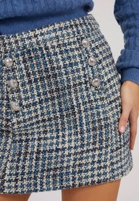 Gewebter blauer und weißer Rock mit strukturierter Oberfläche, silbernen Knöpfen an der Seite und einem geraden Saum.