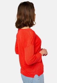 Pull léger rouge à coupe ample, col rond et manches trois quarts, avec des poignets côtelés et un design à ourlet hi-lo.