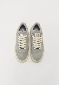Grå sneakers laget av semsket skinn og lær, med perforerte detaljer, kremfargede snører og en logo-patch på tungen. Flat gummisåle.