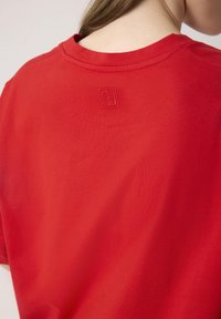 Piros pamut póló kerek nyakkivágással, rövid ujjakkal és egy kis dombornyomott logóval a hátsó oldalon. Simma textúra, laza dizájn.