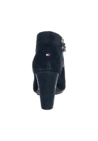 Černé semišové kotníkové boty s vrstveným podpatkem, bočním zipem a malým červeným, bílým a modrým logem na zadním podpatku.