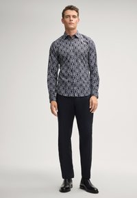 Slim-fit zwart-wit gestreept overhemd met een button-down kraag, gecombineerd met zwarte broek en zwarte leren laarzen.