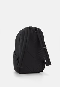 Czarna plecak z wyściełaną teksturą, wzorem chevron, regulowanymi paskami i metką z logo. Zaprojektowany z myślą o komforcie i użyteczności, widoczna kieszeń boczna.