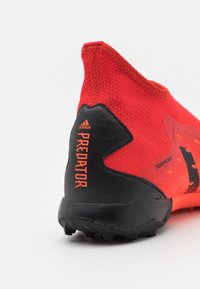Scarpa sportiva di un vivace rosso con una tomaia in maglia testurizzata e un tacco in gomma nera. Presenta un marchio ben visibile e un design distintivo sul lato.