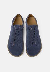 Navy blue suede sneakers with a rounded toe, lace-up design, and tan details. Soft texture, rubber sole with a contrasting brown edge.