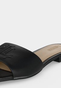 Sort åben tå slide-sandal med lav hæl og præget logo på den brede rem, beige indersål med trykt mærkenavn.