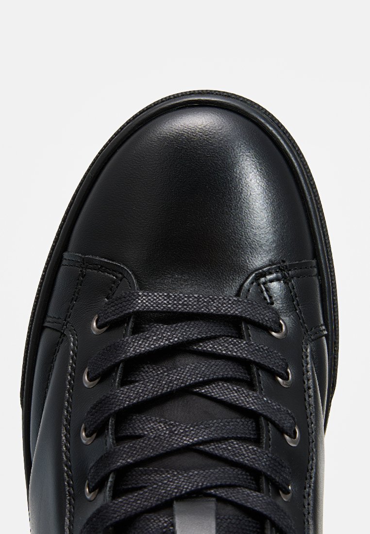 Baskets en cuir noir avec une finition lisse et brillante, un bout rond et des lacets noirs sur une languette texturée avec un minimum de détails de couture.