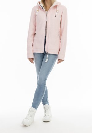 Hellrosa Fleecejacke mit Reißverschluss und Kapuze, mit Seitentaschen und strukturiertem Stoff. Getragen mit hellblauen Skinny-Jeans und weißen Turnschuhen.