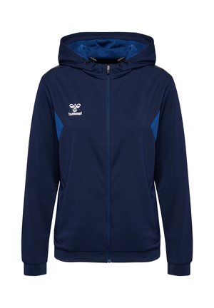 Granatowa bluza z kapturem na zamek błyskawiczny z regulowanymi troczkami, jaśniejsze niebieskie boczne panele, przednie kieszenie i białe logo hummel na lewej piersi.