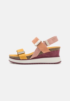 Las sandalias de cuña presentan una combinación de gamuza amarilla, rosa y marrón, con dos correas ajustables y una plantilla texturizada sobre una suela de plataforma blanca.