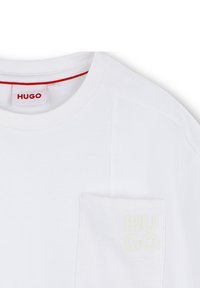 T-shirt bianca in cotone con colletto girocollo a costine, maniche corte e tasca sul petto con logo "HUGO" in giallo chiaro. Etichetta rossa all'interno.