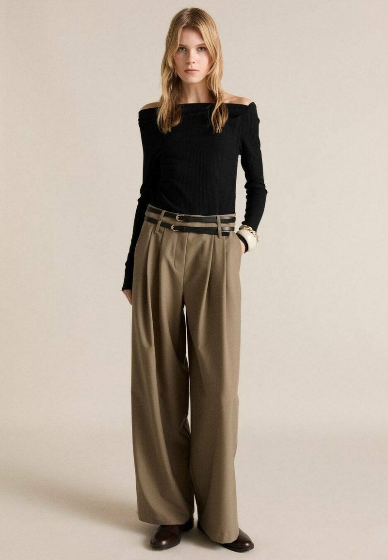 Haut noir à épaules dénudées en maille côtelée associé à un pantalon beige à jambes larges, avec une taille à double ceinture et des chaussures marron. Textures lisses tout au long.