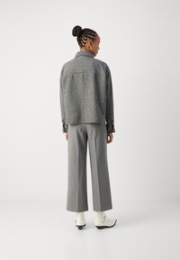 Gray checkered jacket with a relaxed fit, paired with high-waisted gray trousers and white ankle boots. Smooth texture, simple design.