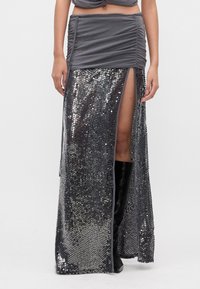 Top gris fruncido con una falda larga que presenta lentejuelas plateadas, una abertura alta y botas negras hasta la rodilla. Textura suave con detalles reflectantes.