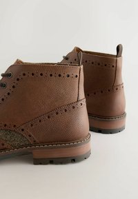 Brown leather ankle boots with a textured finish, decorative perforations, herringbone side panel, and a sturdy rubber sole.