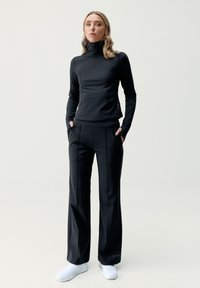 Juodas sportinis kostiumas, susidedantis iš prigludusios ilgomis rankovėmis polo marškinėlių ir plačių kelnių su šoninėmis kišenėmis, derinamas su baltais taip pat patogiais batais.