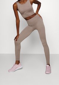Top corto acanalado beige y leggings de cintura alta a juego, combinados con zapatillas deportivas rosas. La tela tiene una textura suave y un diseño ajustado.