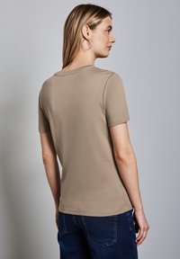 Lyhythihainen beige t-paita, joka on valmistettu puuvillasta. Paitassa on pyöreä pääntie ja sileä pinta, joka on yhdistetty sinisiin farkkuihin. Yksinkertainen muotoilu.
