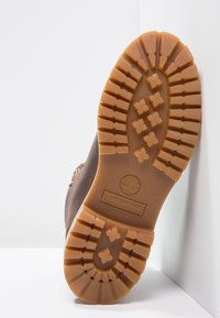 Hnědá podrážka Timberland boty vyrobená z robustního, strukturovaného gumového materiálu. Má výrazné vzory vzorku a viditelné logo.