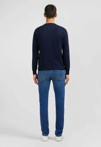 Pull en tricot bleu marine avec un col rond et des manches longues, associé à un jean bleu clair avec un design classique à cinq poches.