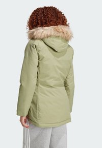 Olivově zelená parka s kapucí podšitou kožešinou, s texturovanou tkaninou, rovnými liniemi a mírně delším zadním lemem.