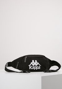 Banane noire en tissu avec fermeture éclair, arborant un logo Kappa blanc et une sangle réglable, texture lisse et design compact.