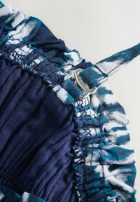 Granatowa sukienka z marszczonym materiałem i białymi akcentami tie-dye, z regulowanym srebrnym paskiem i falbaniastym dekoltem.