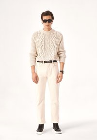 Jersey crema con patrón de cable texturizado, pantalones crema, cinturón negro, zapatillas altas negras y gafas de sol oscuras.