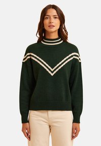 Maglione verde a maglia con colletto alto, caratterizzato da strisce a zig zag bianche in contrasto sul petto. I polsini e l'orlo a coste aggiungono texture.