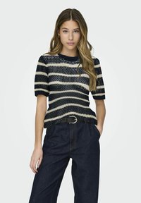 Pull en tricot à rayures bleu marine et crème, à manches courtes et col rond, associé à un pantalon en denim foncé taille haute et une ceinture noire.