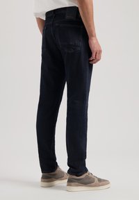 Pantalones de mezclilla con un lavado oscuro, diseño de pierna recta y costuras sutiles. Llevados con zapatillas casuales de color claro.
