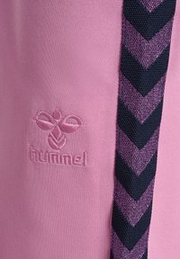 Różowy materiał z haftowanym logo hummel oraz pionowymi granatowo-fioletowymi wzorami w jodełkę.