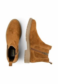 Tan ruskinds ankelstøvler med lynlås detalje på siden, tekstureret overdel og en tykk, rillede beige sål for stabilitet og støtte.