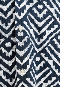 Άσπρο γεωμετρικό σχέδιο ζιγκ-ζαγκ σε σκούρο μπλε υφή υφάσματος με δύο μικρά άσπρα στρογγυλά κουμπιά ραμμένα κατακόρυφα.