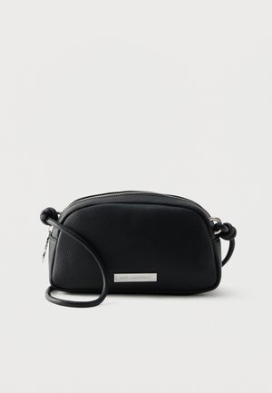 Kleine zwarte leren crossbody tas met verstelbare riem en zilveren rits, voorzien van een metalen logoplaatje aan de voorkant.
