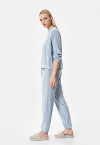 Conjunto de loungewear azul claro con un acabado texturizado, que incluye una camiseta de cuello redondo y pantalones con cordón, combinados con suaves pantuflas beige.
