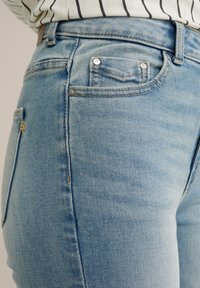 Helle blaue Jeans aus Denim mit einem taillierten Design, ausgestattet mit einer vorderen Tasche, metallischen Beschlägen und dezenten Nähdetails.